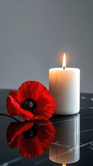 A lit candle beside a red poppy, reflecting on a black marble surface