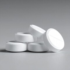 Four white tablets, stacked and scattered, on a plain gray background
