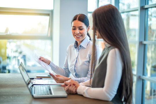 Female colleagues discussing business strategy while reviewing documents in bright modern office