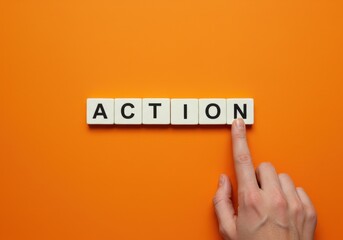 A hand pressing a letter tile to spell the word ACTION on an orange background