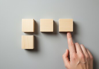 A hand pointing to one of four wooden blocks on a gray background
