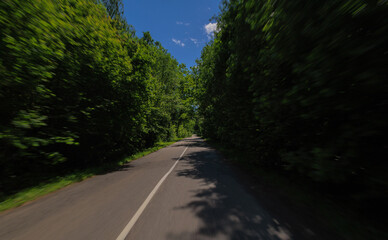 Obraz premium The effect of speed on the road and blurred objects. View of the road on a sunny summer day.