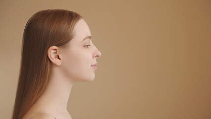 Profile view of a young woman with clear skin and long well-groomed hair against a neutral backdrop. Aesthetic medicine, dermatology, haircare and natural beauty. Hair salon ads. Copy space 