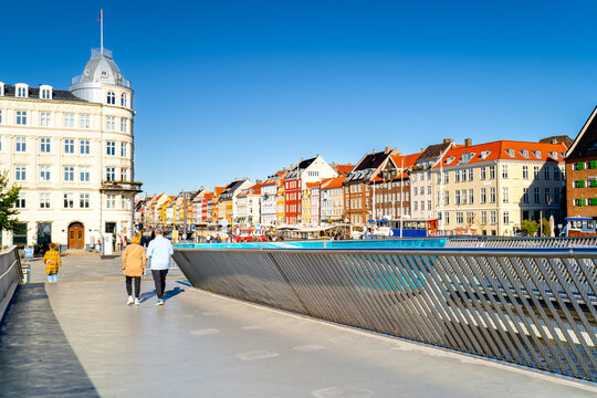 People walk on Inderhavnsbroen Bridge in Copenhagen, with with colorful urban architecture. 
Life on street  Scandinavian seaside town, Denmark. - Powered by Adobe