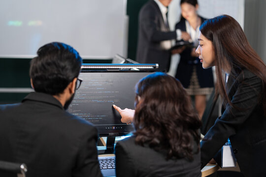 A diverse team of software developers examining computer code on a monitor, focusing on debugging or code review. Mentorship, technical training. Developing application program, Cybersecurity center