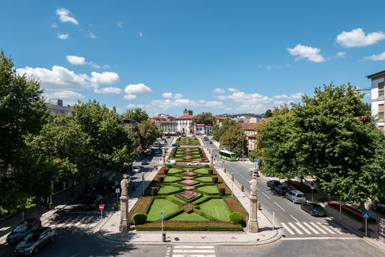 Vista panor&acirc;mica do jardim da Alameda da Rep&uacute;blica em Guimar&atilde;es, apresentando sebes de buxo formalmente talhadas e canteiros de flores, ladeados por est&aacute;tuas e edif&iacute;cios tradicionais em Portugal
