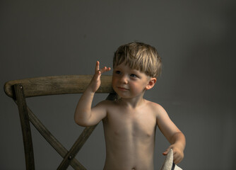 Two-year-old boy sitting on a chair wearing a hat, no shirt