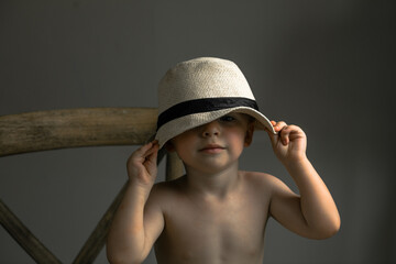 Two-year-old boy sitting on a chair wearing a hat, no shirt
