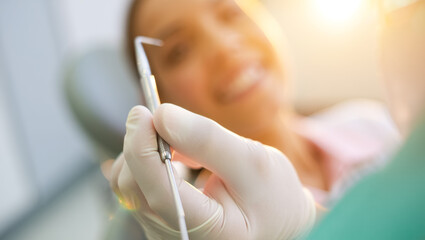 Close-up of a dentist&rsquo;s gloved hand holding a dental tool with a blurred smiling patient in the background, symbolizing oral health, professional care, and a positive dental visit atmosphere
