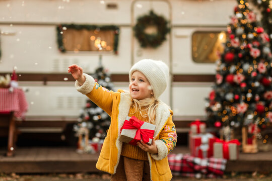 little girl looks up and waits for the first snow and celebrates Christmas near the trailer with Christmas decorations