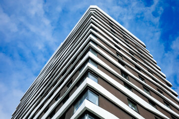 A modern multi-story building with a brown and white façade, clean lines, and large windows. The architectural style is minimalist, emphasizing geometry and functionality.
