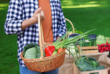 Man with different vegetables in wicker basket at farmer's market, closeup