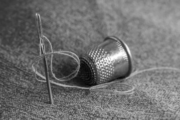 A needle and thread, a tape measure, and a thimble are lying on the fabric. Sewing supplies