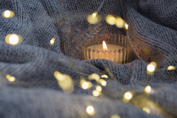 Cozy atmosphere with candle, knitted blanket and soft lighting. Bokeh effect.