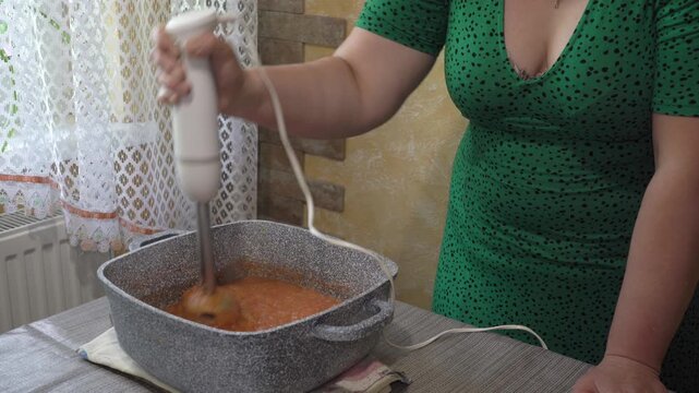 attractive woman working with a blender, woman at the table chopping vegetables for a sauce with a blender
