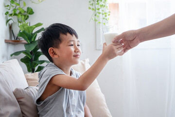 Asian Mother Giving a Glass of Milk to Her Son at Home, Teaching Healthy Habits and Nutrition, Showing Family Love, Care, and a Balanced Lifestyle for Kids