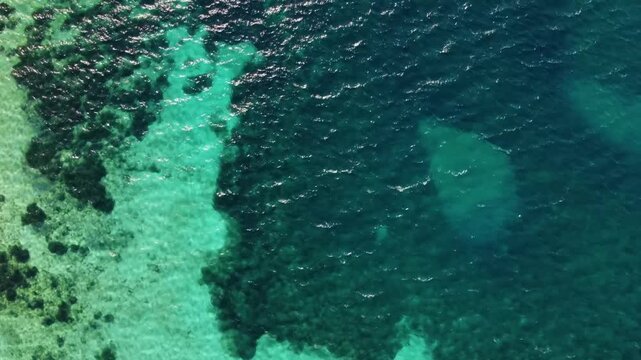 aerial perspective captures the crystal clear turquoise waters of the Mediterranean Sea, transitioning into deeper blue hues along the coast near the ancient city of Knidos, Turkey. The footage showca