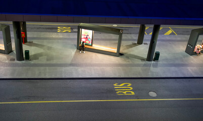 Urban bus station at night with illuminated shelters and a lone passenger waiting for transportation