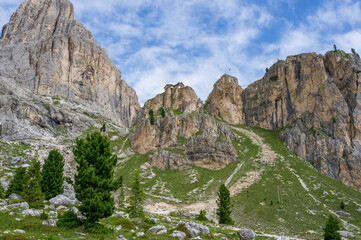Majestic mountain landscape with rocky cliffs and lush greenery under a bright blue sky in the Dolomites