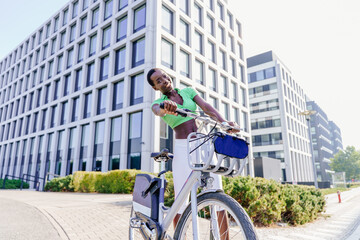 Obraz premium Happy Black woman leaning on bicycle handlebars in city environment