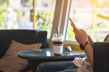 Hands of happy man using cell phone sitting on couch at home. View of man looking at smartphone on display. Man holding mobile phone indoors. Communication, lifestyle and modern domestic life concept.