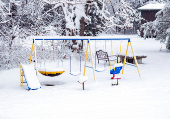 The charm and quietness of a swing set with no children yet covered in a blanket of magical white powdery snow caps. A scenic rustic backdrop adds to the tranquility. Bokeh.