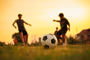 Silhouette action sport outdoors of a group of kids having fun playing soccer football for exercise at the green grass field under the twilight sunset sky.