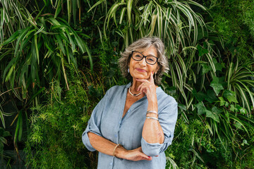 Senior woman smiling, looking at camera, standing by vertical garden