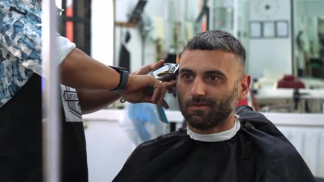Electric clipper haircut by barber, frontal perspective
