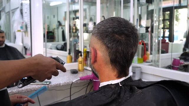 Electric clipper haircut from back by professional barber
