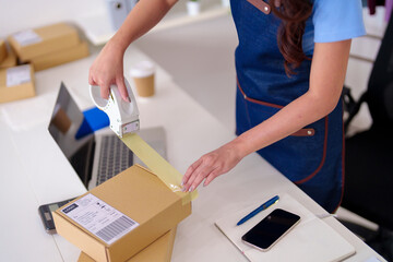 Adult female entrepreneur packing ecommerce orders for shipping at home office ensuring efficient...
