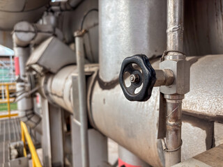 Close-up showcases a black valve on metallic pipes, part of an industrial or manufacturing system.