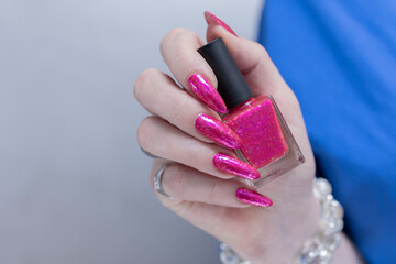 Female hand with long nails and a bottle bright neon pink fuchsia color nail polish