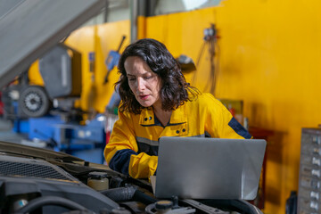 female mechanic or engineer in workwear using laptop checking car engine to diagnostic and repair in auto services
