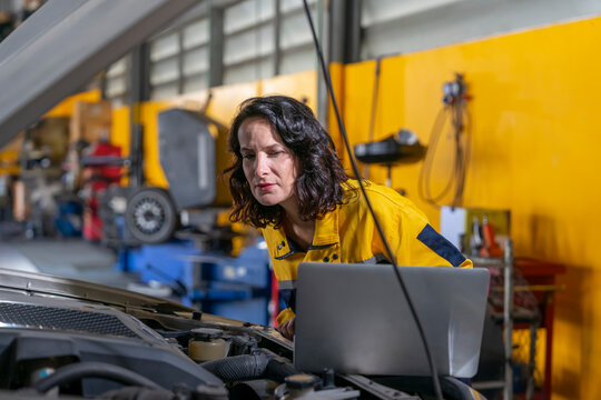 female mechanic or engineer in workwear using laptop checking car engine to diagnostic and repair in auto services