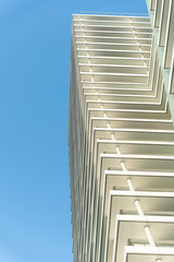 Obraz premium Tall modern building with geometric balconies and white structural lines, from below on a clear blue sky. For illustrating urban architecture, construction, or real estate development concepts.