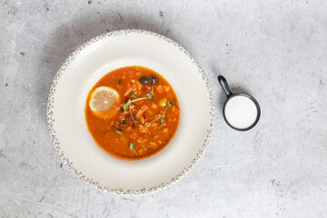Rich soup with smoked meats, sausages, lemon, and olives, viewed from above on a gray background