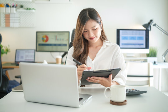 Cheerful woman taking notes on a clipboard in modern office setting.