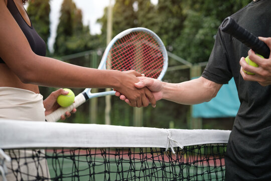 Close up of tennis players shaking hands over the net after match, symbolizing respect and sportsmanship.