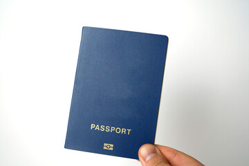 Hand holding a blue biometric passport against a plain white background, symbolizing identity,...