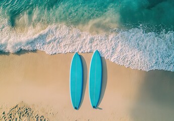 Obraz premium A real photo of two blue surfboards placed upright on a sandy beach with turquoise waves crashing in the background under a clear sky