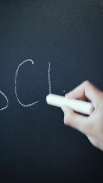 Teacher writing word school with white chalk on blackboard. Vertical video