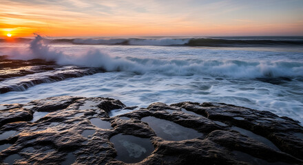 Obraz premium Ocean waves crashing against rocky shore at sunset