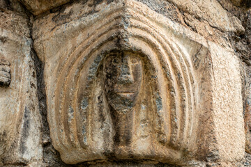 Close-up of a weathered Romanesque capital depicting a human face, an architectural detail of the historic Sant Lliser d'Al&oacute;s d'Isil church in the Spanish Pyrenees. Catalonia
