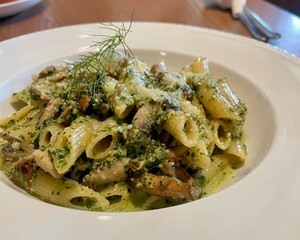 Delicious penne pasta with creamy pesto sauce, mushrooms, and herbs served in a white bowl, perfect for an Italian dining experience.