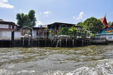 Stilt houses on the Chao Phraya River in Bangkok, Thailand. Contrast of traditional dwellings and a modern skyscraper.