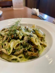 Delicious penne pasta with creamy pesto sauce, mushrooms, and herbs served in a white bowl, perfect for an Italian dining experience.