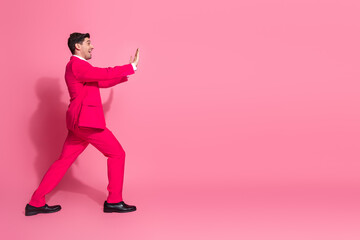 Energetic young man in vibrant pink suit posing playfully against vivid pink background expressing charm and confidence
