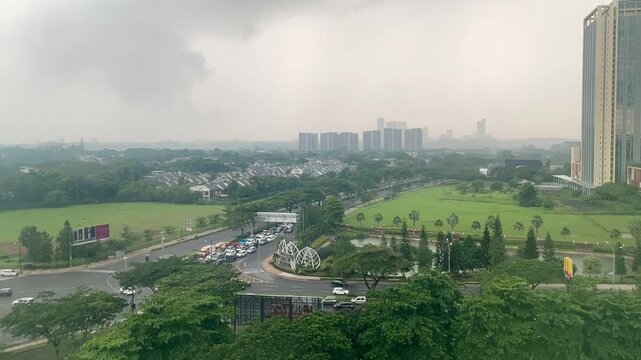 Overcast skyline and modern cityscape after rainfall, with green fields, high-rise buildings, and wet streets under cloudy skies.