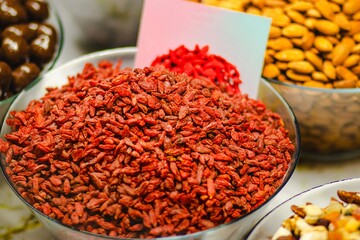 Vibrant assortment of dried goji berries in a glass bowl, surrounded by various nuts and seeds, showcasing healthy snack options and colorful textures in a market setting